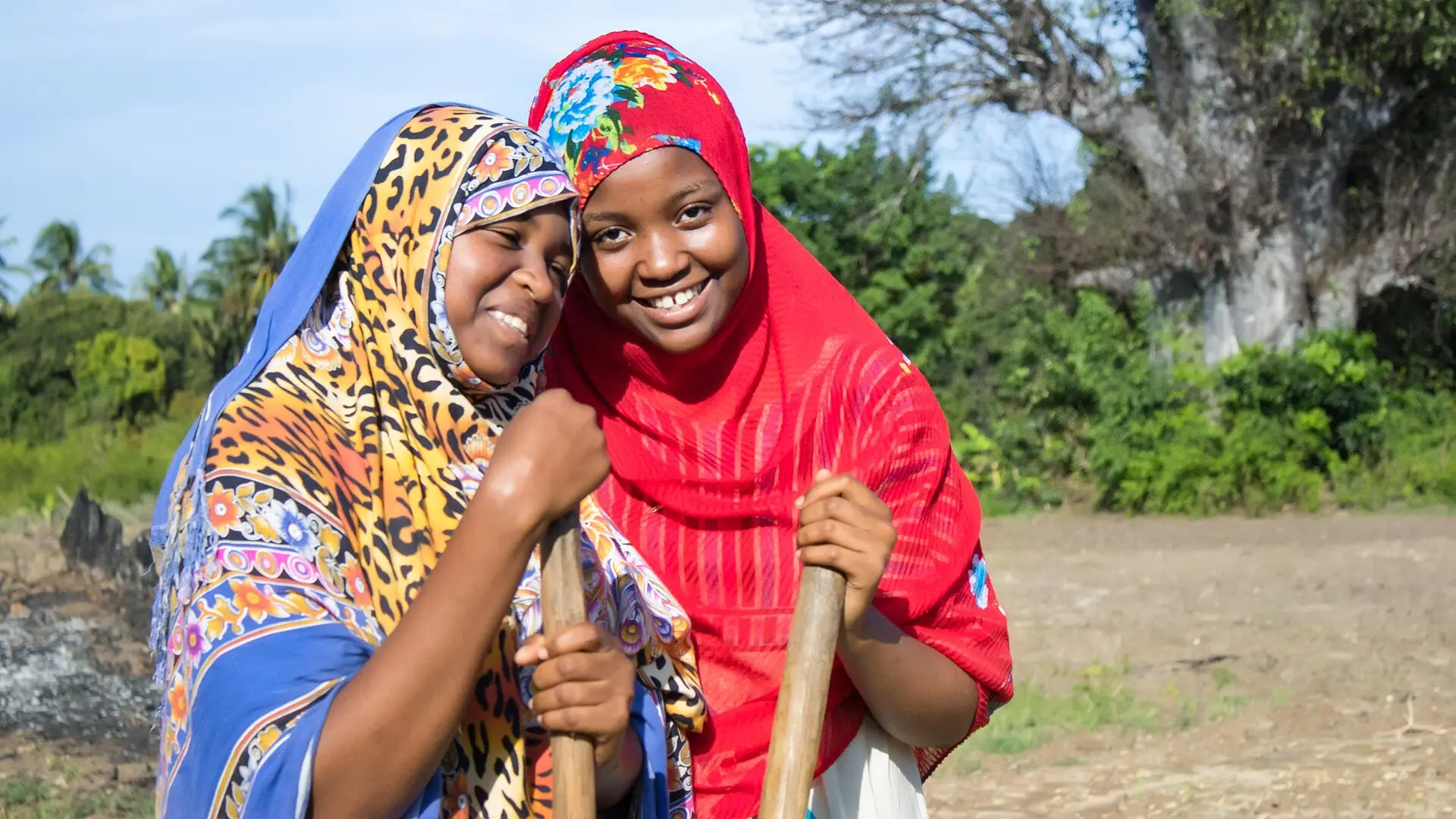 Two smiling women farmers holding hoes